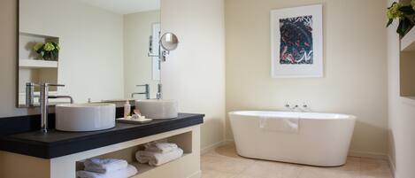 A modern bathroom with two sinks, a large mirror, a bathtub, and a framed artwork on the wall.