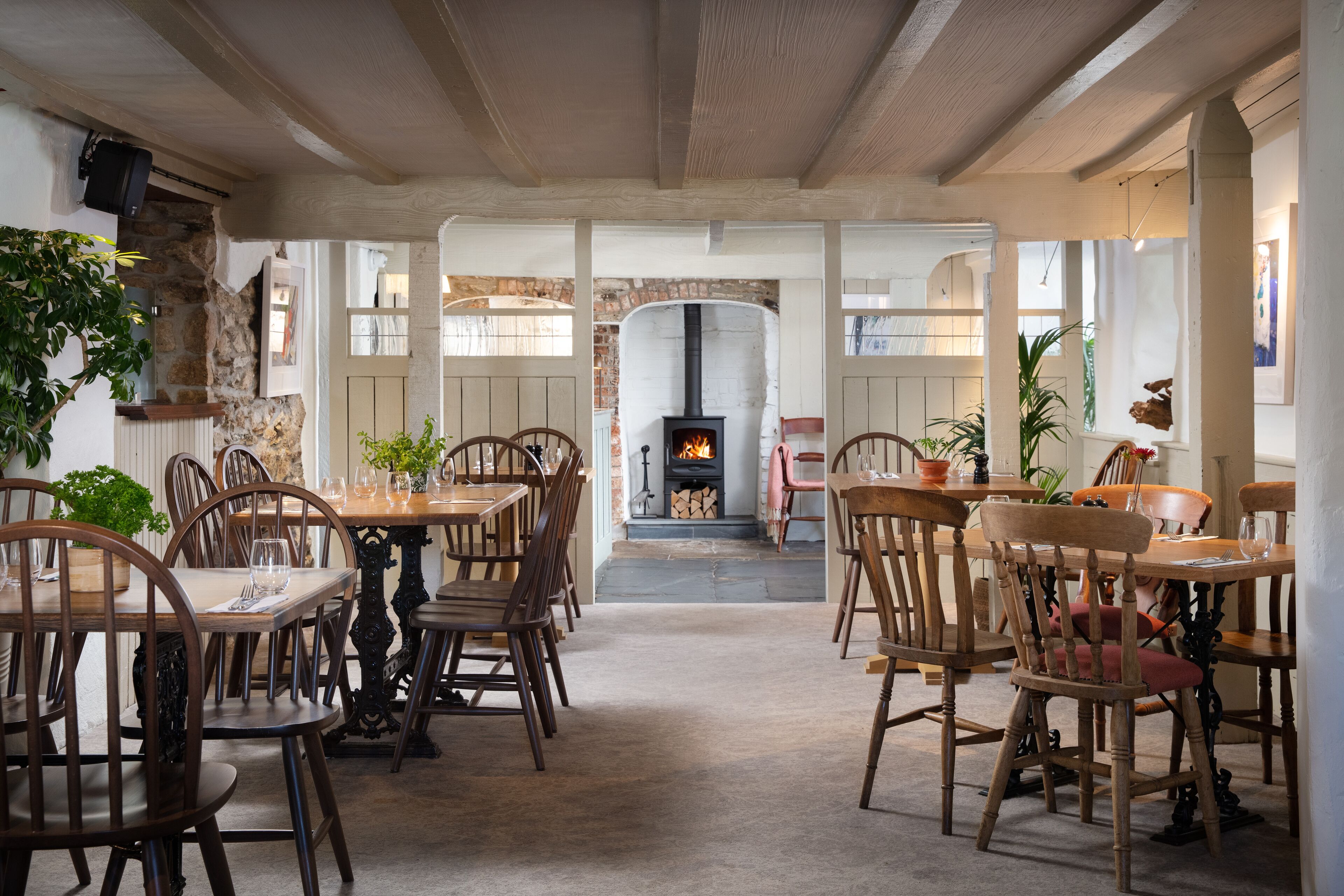 A cozy dining area with wooden tables and chairs, a stone wall, and a fireplace.