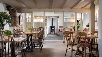 A cozy dining area with wooden tables and chairs, a stone wall, and a fireplace.