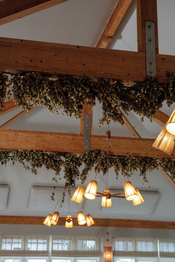 A room with exposed wooden beams, hanging lights, and a garland of dried flowers. - The Plume of Feathers (Newquay)