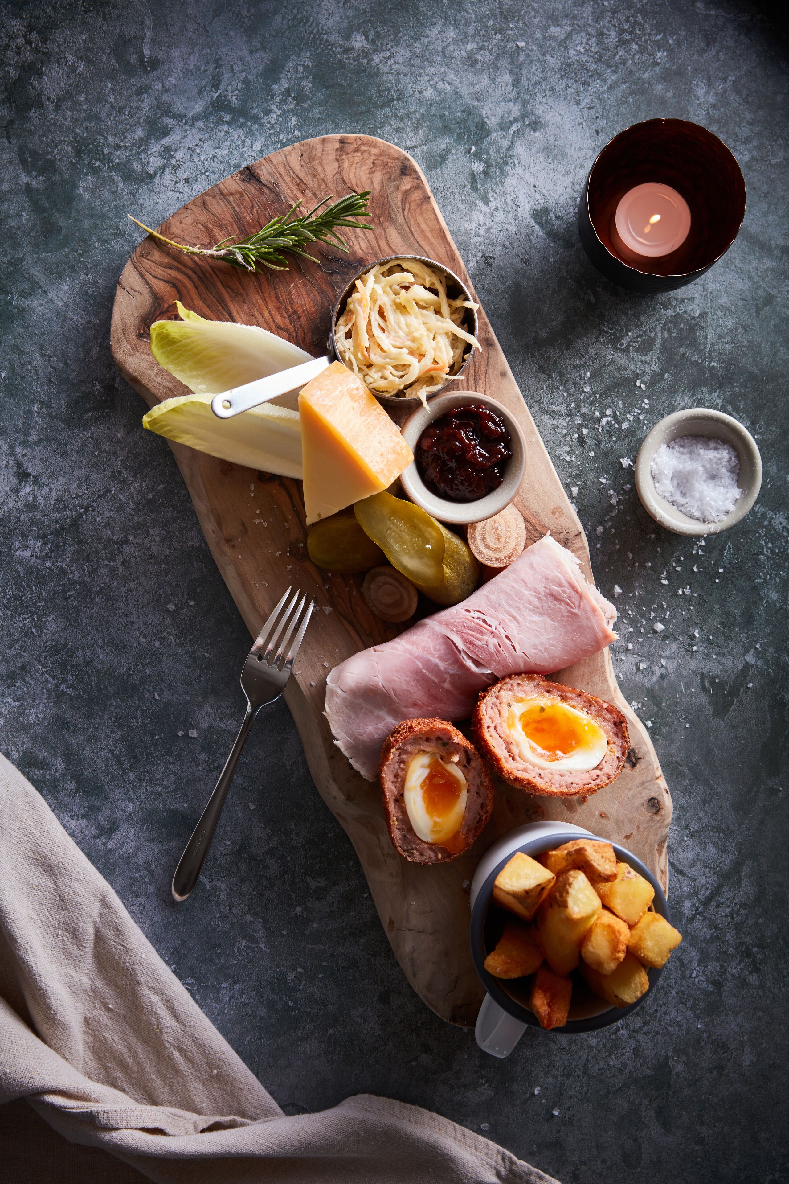 A wooden board with various food items including cheese, pickles, and a boiled egg.