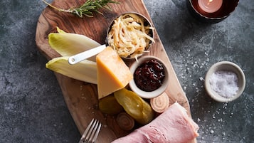 Una tabla de madera con varios alimentos, incluyendo queso, pepinillos y un huevo duro.