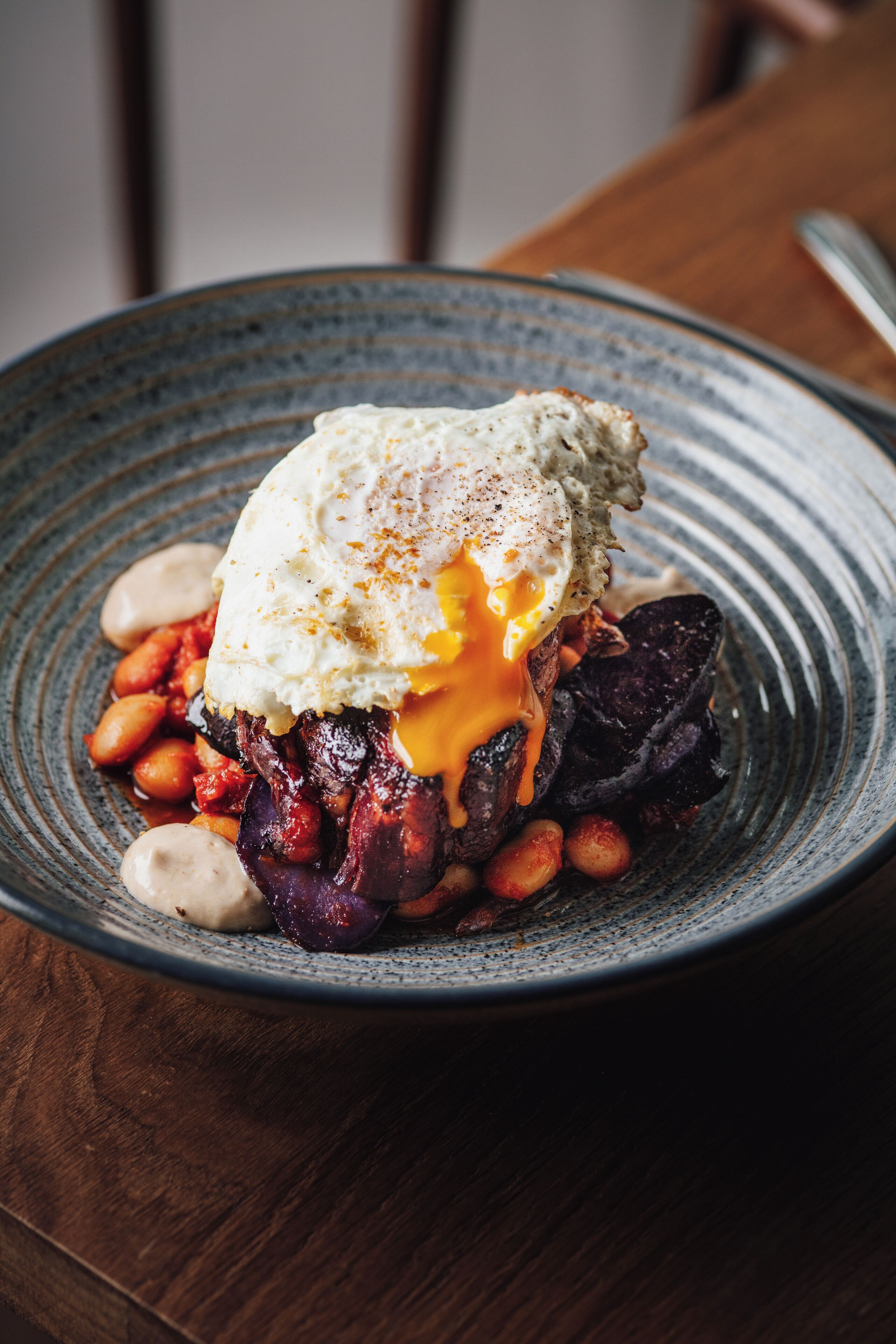 A plate with a poached egg, beans, and a piece of meat on a ceramic plate.