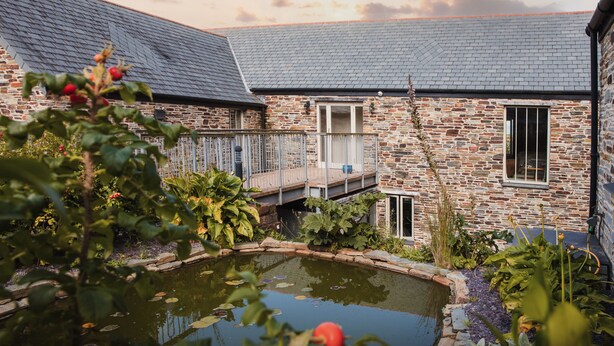 A stone building with a small pond, surrounded by greenery and a wooden deck. - The Plume of Feathers (Newquay)