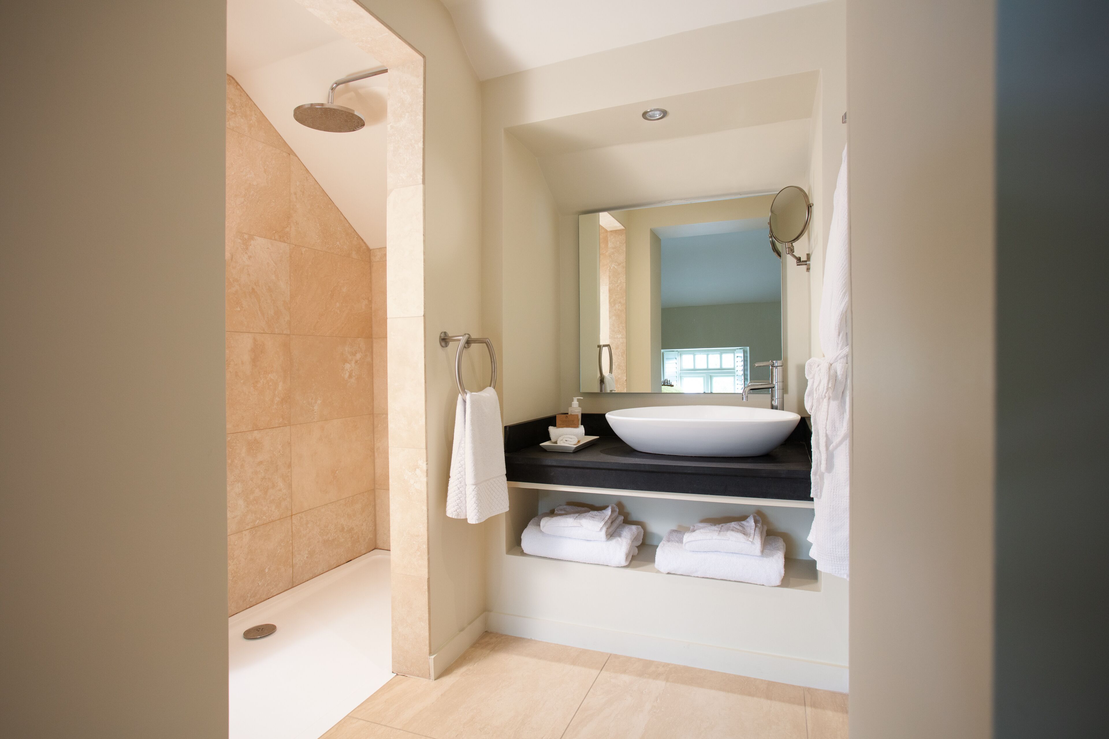 A modern bathroom with a large bathtub, a sink with a mirror, and neatly folded towels on a shelf.