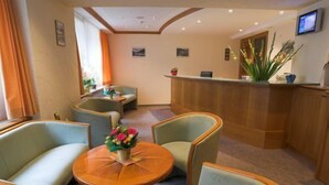 A hotel lobby with a reception desk, seating area, and a small table with flowers. - Hotel Heilquelle (Leukerbad)