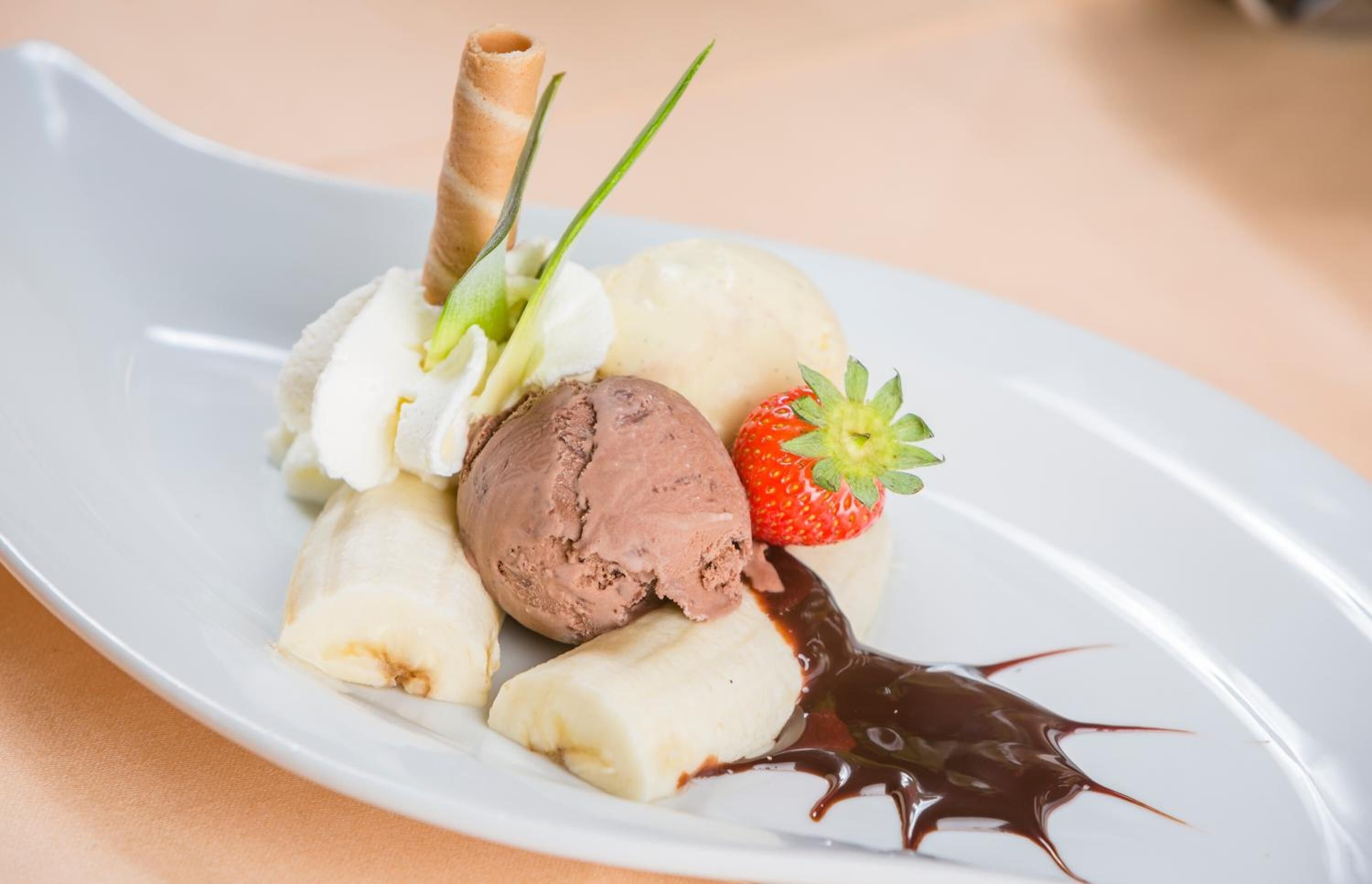 A dessert plate with ice cream, a strawberry, and chocolate sauce.