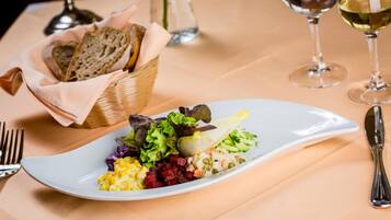 Une assiette blanche contenant une salade colorée, un panier de pain et un verre de vin blanc, le tout posé sur une table.