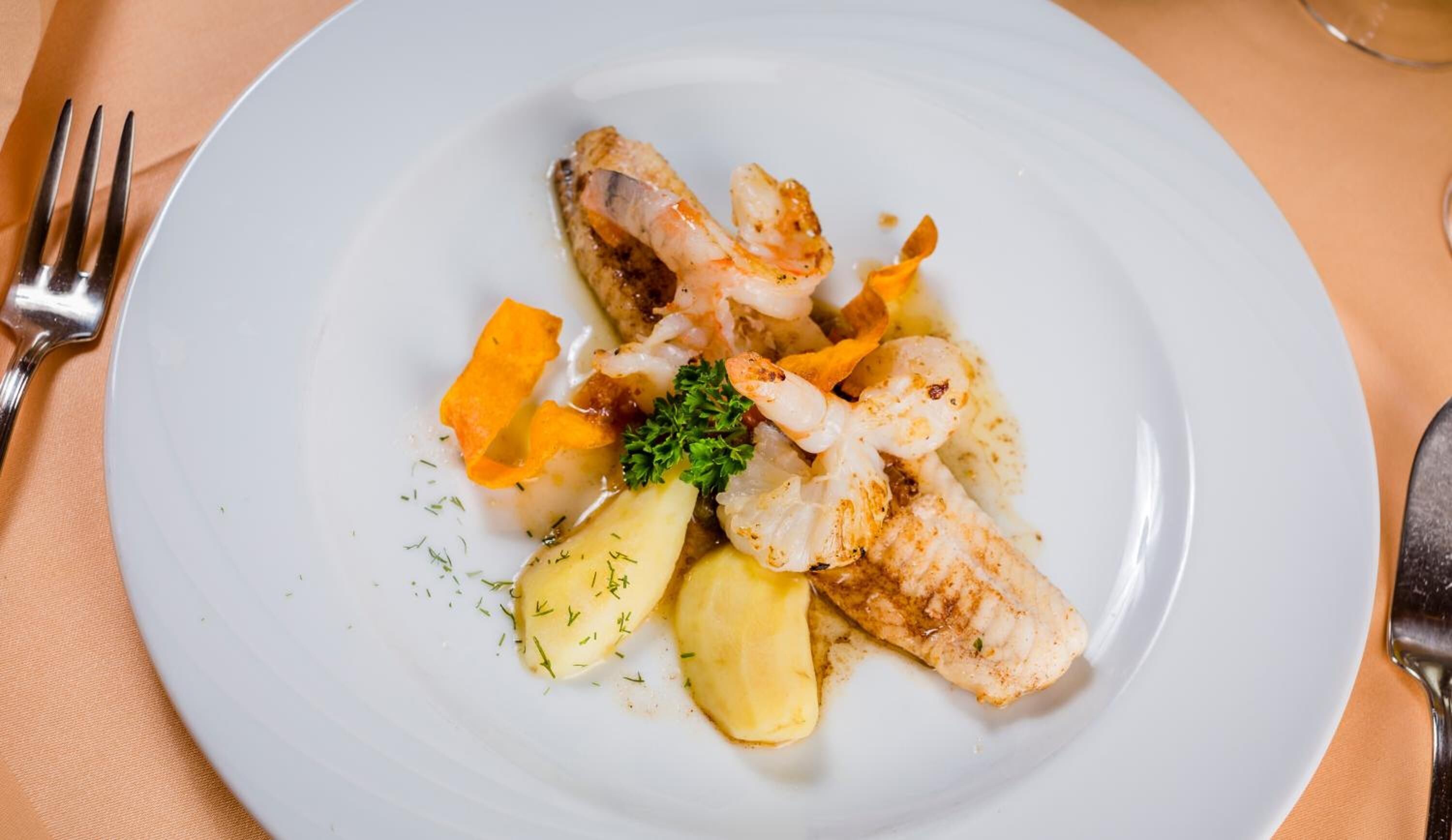 Prato com peixe grelhado, batatas e cenouras, decorado com salsa.