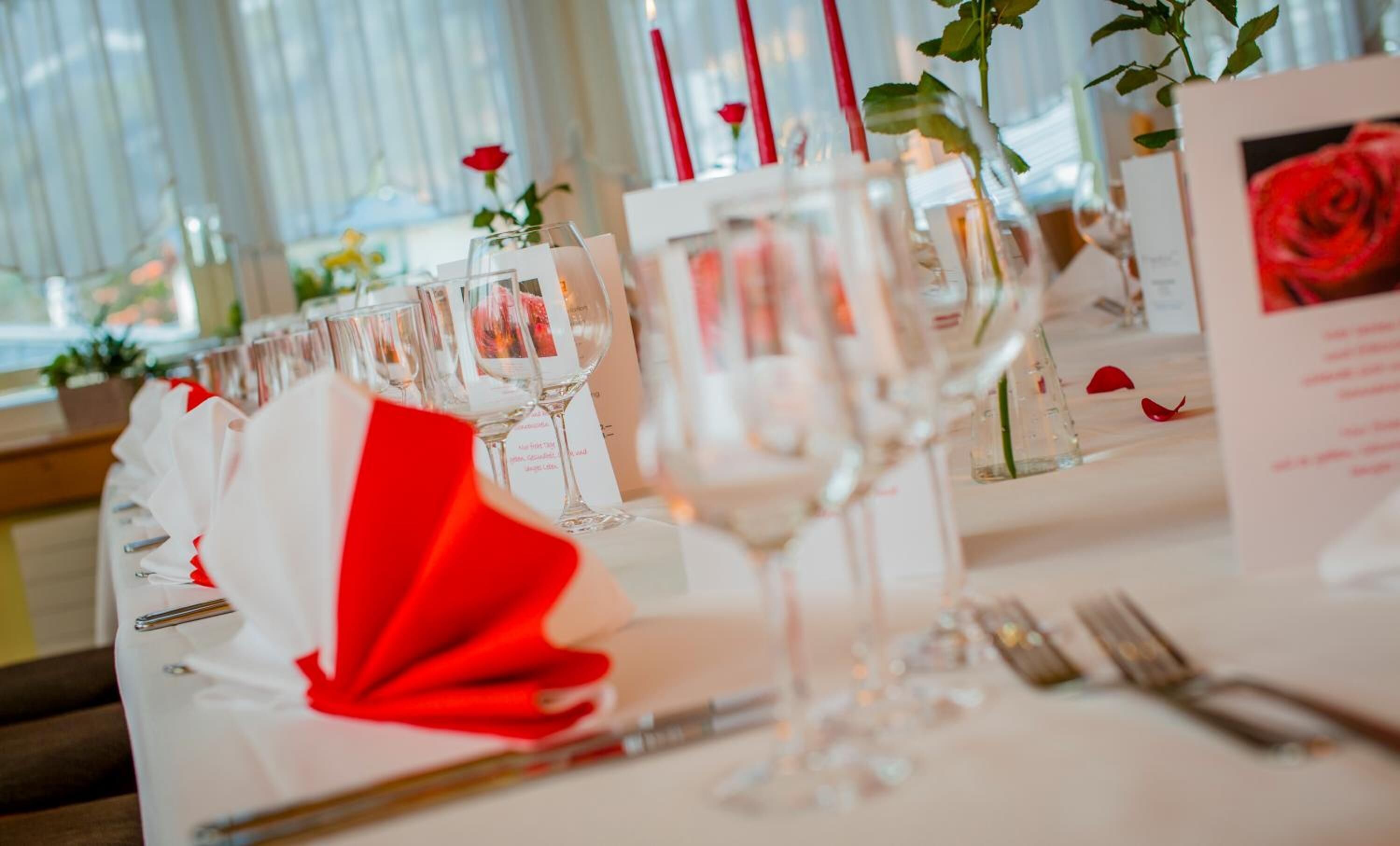 Une table dressée pour un événement formel, avec de la belle verrerie, un menu et des décorations à base de roses rouges.