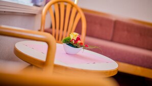 A small table with a white bowl containing a bouquet of flowers, a pink placemat, and a wooden chair with a curved backrest. - Hotel Heilquelle (Leukerbad)