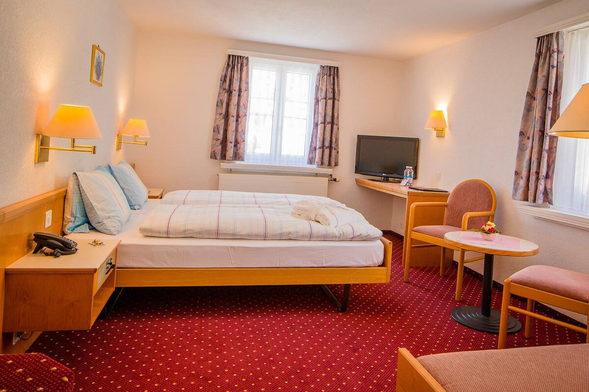 Une chambre d’hôtel comprenant un lit, un bureau avec une télévision, deux chaises, une petite table et un téléphone sur la table de chevet.