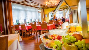 A restaurant with wooden furniture, red tablecloths, and a fruit bowl on the table. - Hotel Heilquelle (Leukerbad)