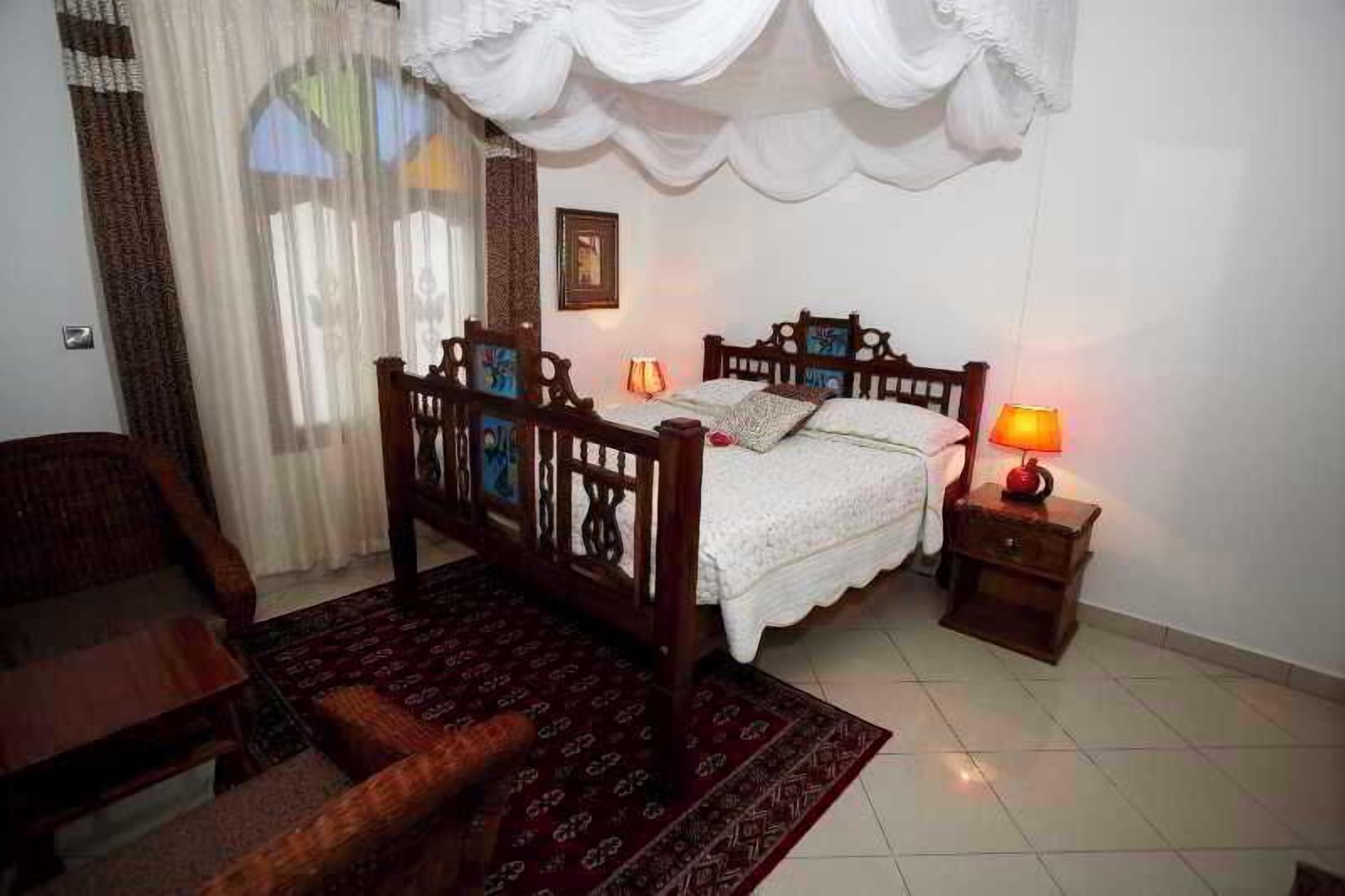 Une chambre à coucher avec un lit en bois, une table de chevet avec une lampe, un tapis à motifs et une chaise.