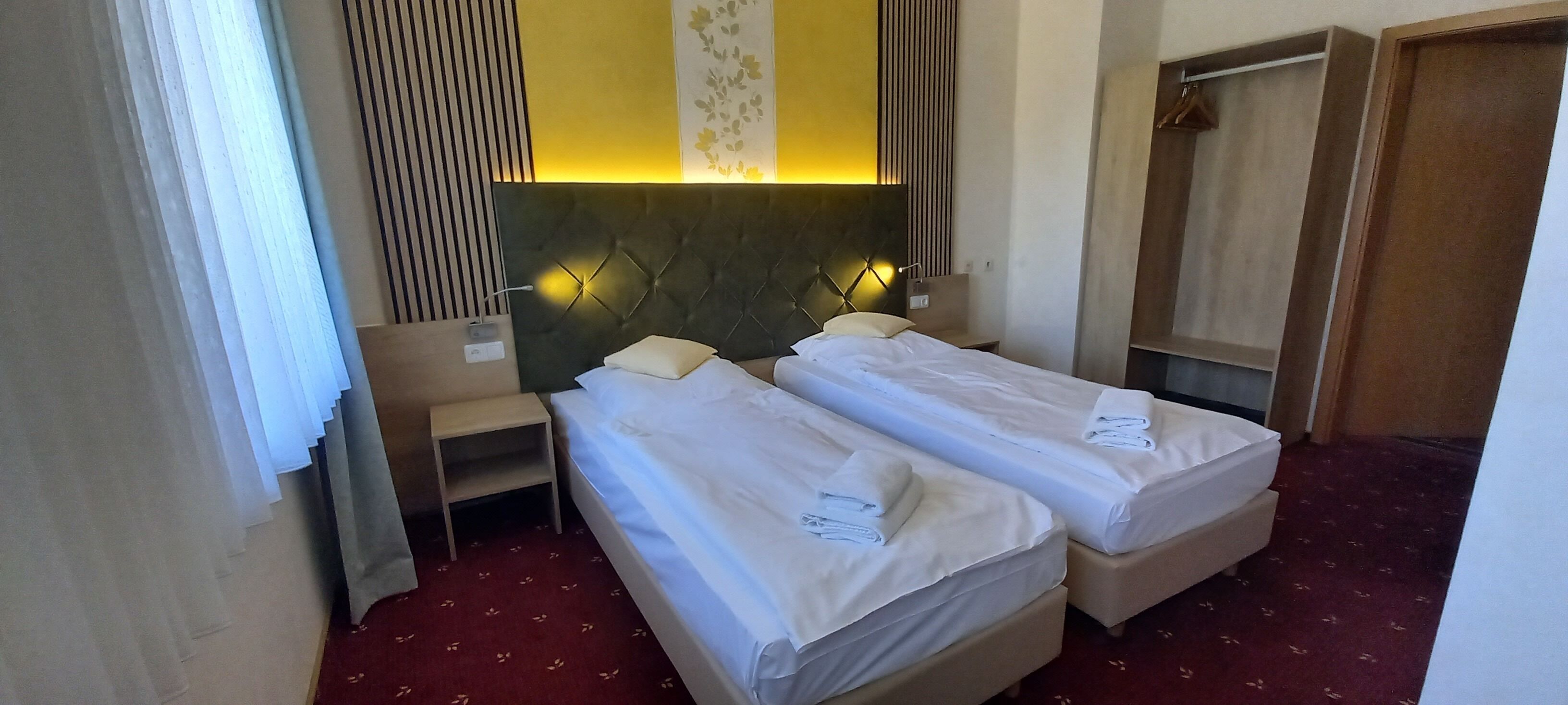 A hotel room with two beds, a nightstand, a lamp, and a wardrobe.