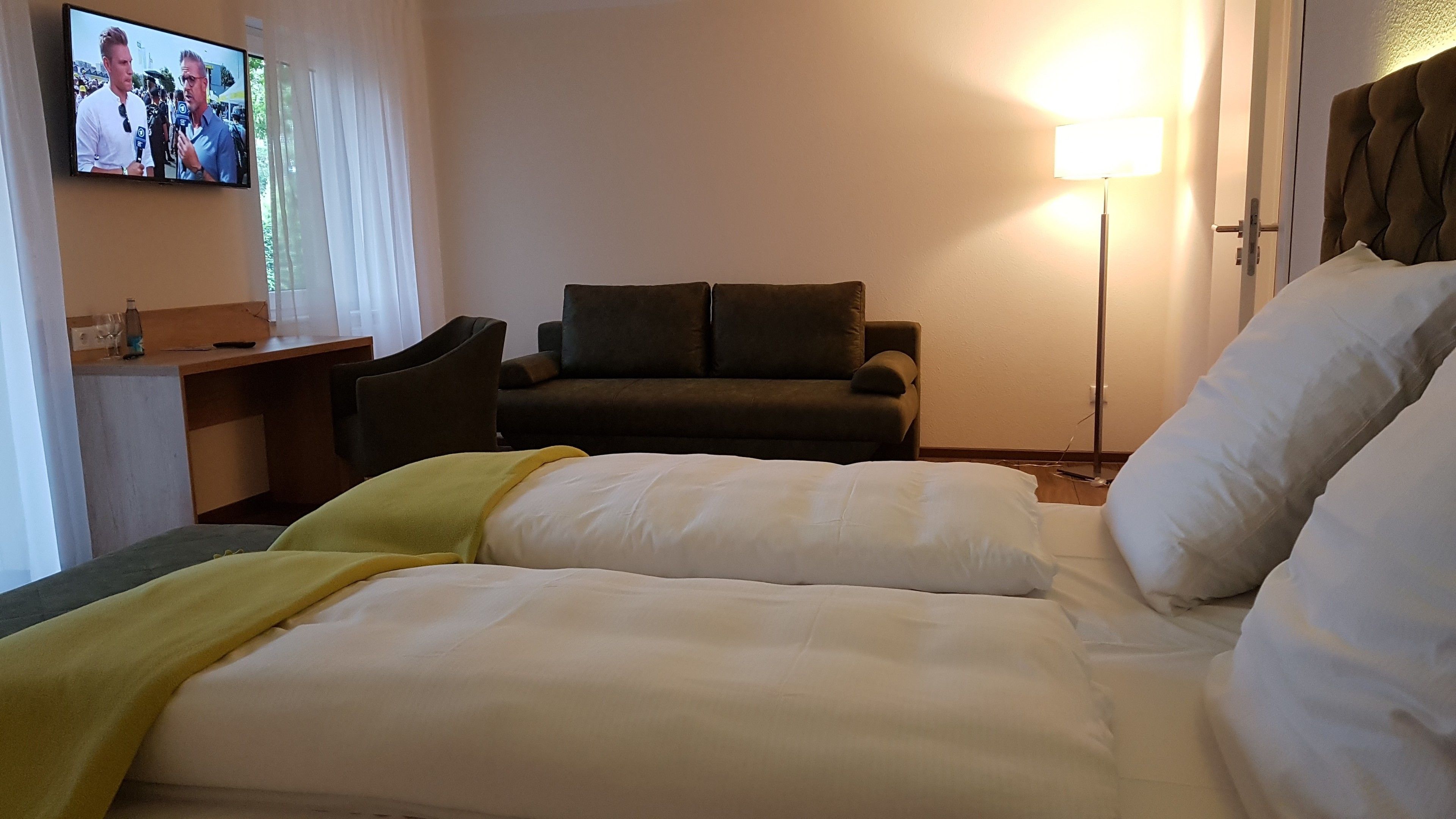 Habitació d'hotel amb un llit, una taula de treball, una cadira i una televisió penjada a la paret.