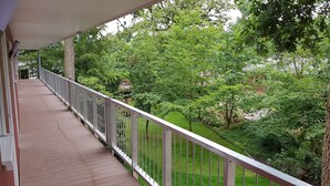 A wooden deck with a white railing overlooking a lush garden with various trees and shrubs. - Kräuterhotel Heidejäger (Rotenburg)
