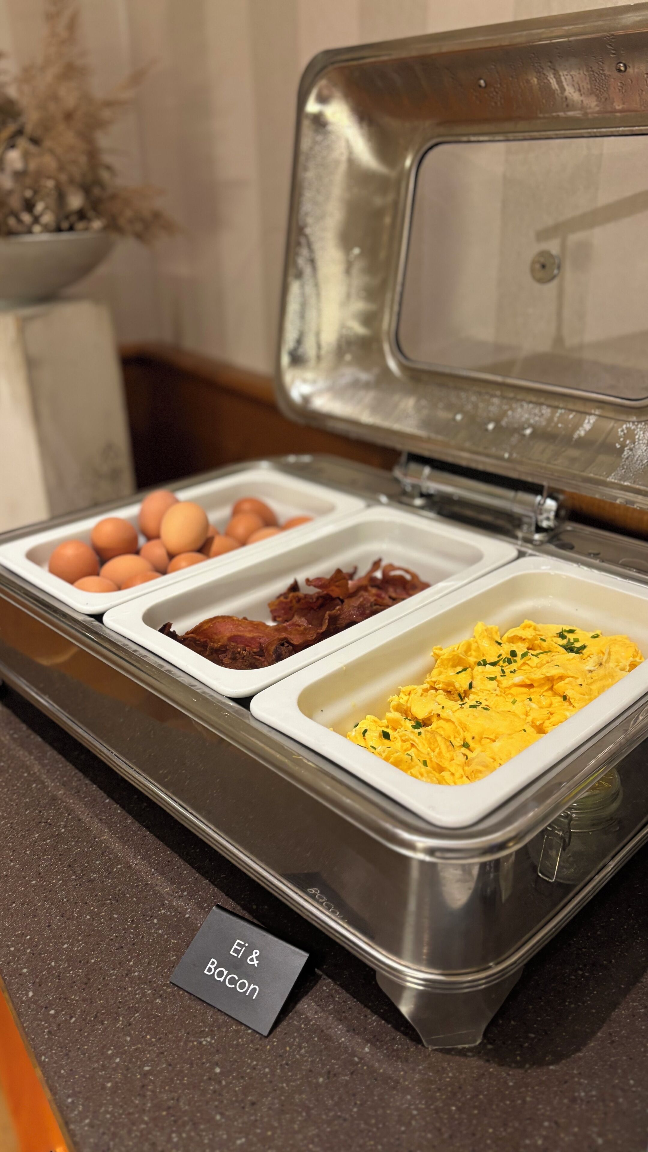 A buffet with labeled sections for eggs, bacon, and scrambled eggs.