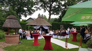 An outdoor event with a brick structure, red tables, and a white carpet path. - Kräuterhotel Heidejäger (Rotenburg)