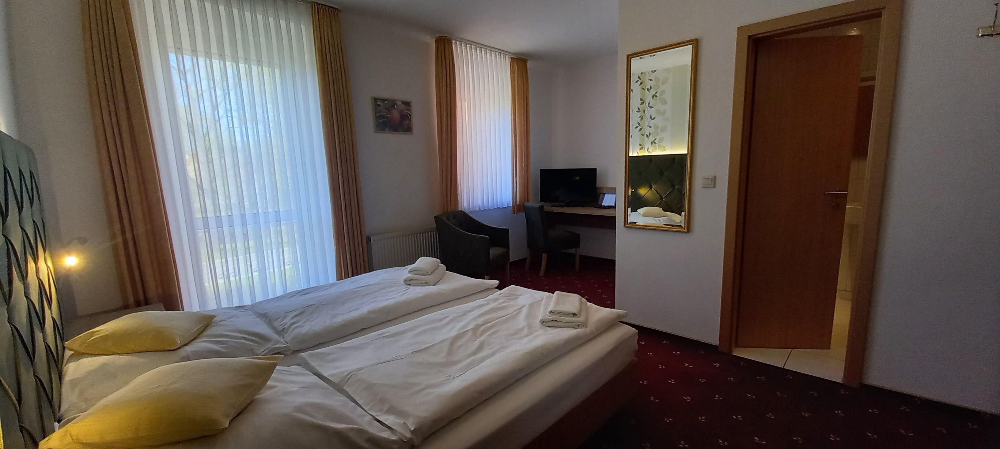 A hotel room with two beds, a desk, a television, and a mirror.