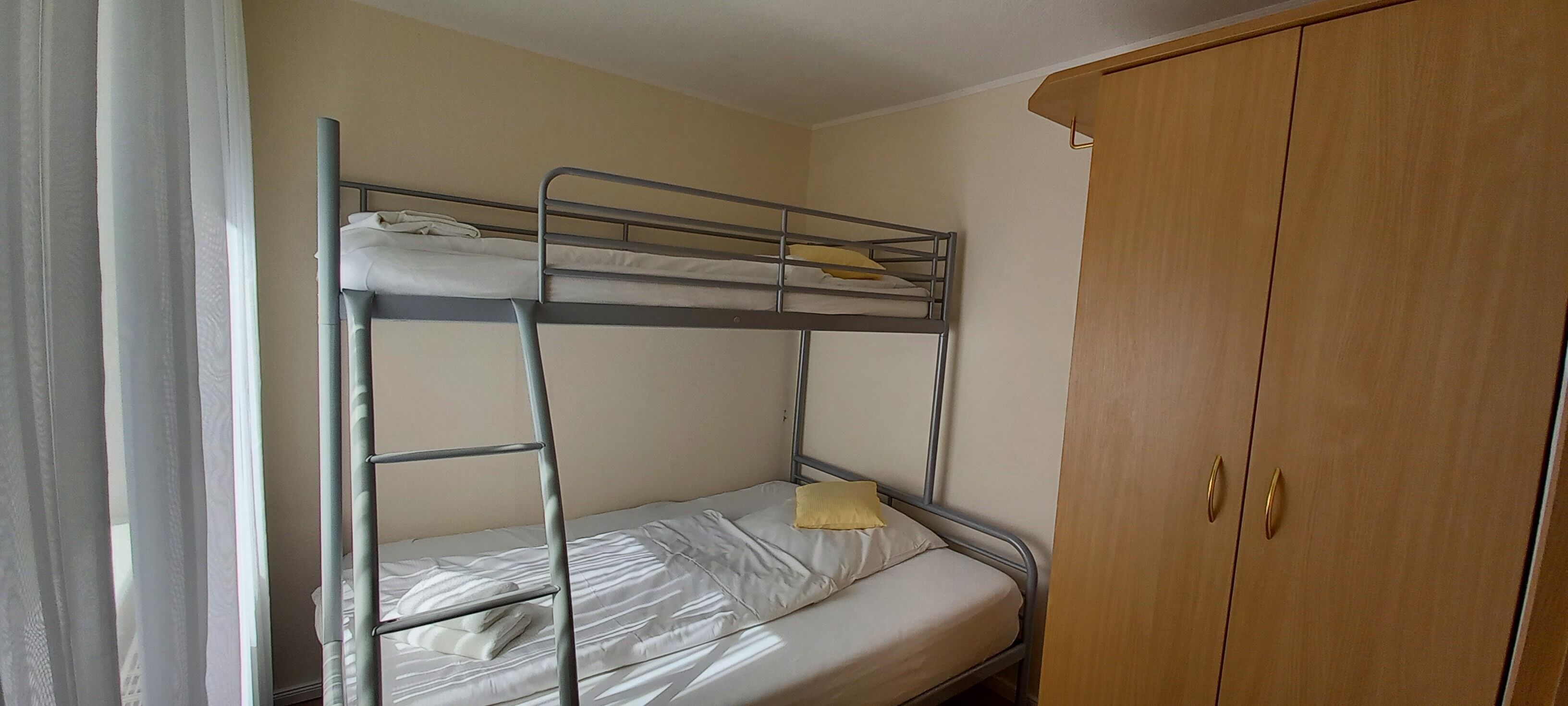 A bunk bed with a wooden wardrobe and a curtain.