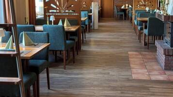 Ein Restaurant mit Holzboden, grünen Polstersesseln und Pendelleuchten.