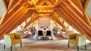 Une chambre mansardée avec un plafond haut et des poutres apparentes. On y trouve une table à manger dressée pour six personnes, entourée de deux canapés et de deux fauteuils.