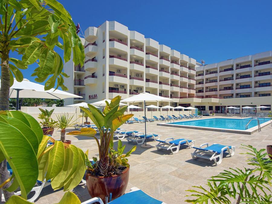 Un hotel con piscina, varios balcones y zonas de estar al aire libre con sombrillas.