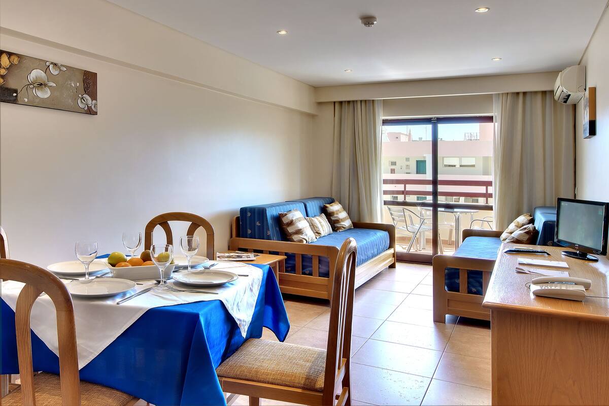 Une pièce comprenant une table à manger dressée pour deux personnes, un canapé, un lit et un bureau avec un ordinateur.