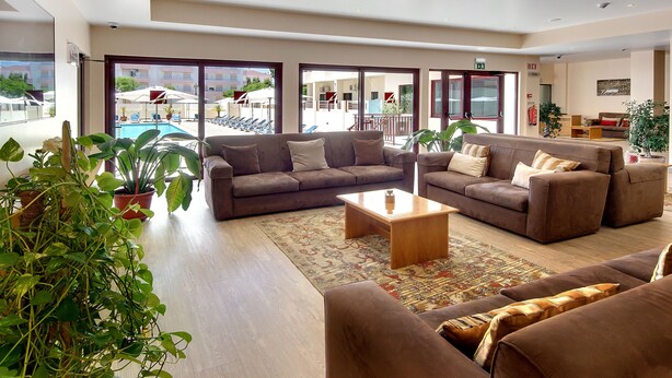 Amplia sala de estar con sofás, una mesa de centro y plantas en macetas. Grandes ventanales ofrecen vistas a una piscina y zona de estar al aire libre.