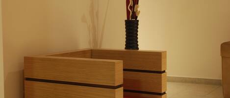 A wooden bench with a red cushion and a vase with branches.