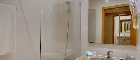A bathroom with a glass shower enclosure, a granite sink, and a mirror reflecting a door and a sink area.