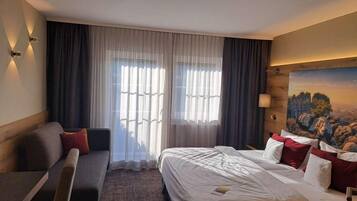 Ein Hotelzimmer mit Bett, einer Couch, einem Gemälde und einem Fenster mit Vorhängen.