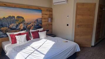 Ein Hotelzimmer mit einem Bett, einem Bild an der Wand, einer Klimaanlage und einer Holztür.