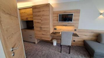 Ein gemütlicher Raum mit einem Holzschrank, einem Schreibtisch mit Stuhl, einem an der Wand befestigten Fernseher und einer Couch.