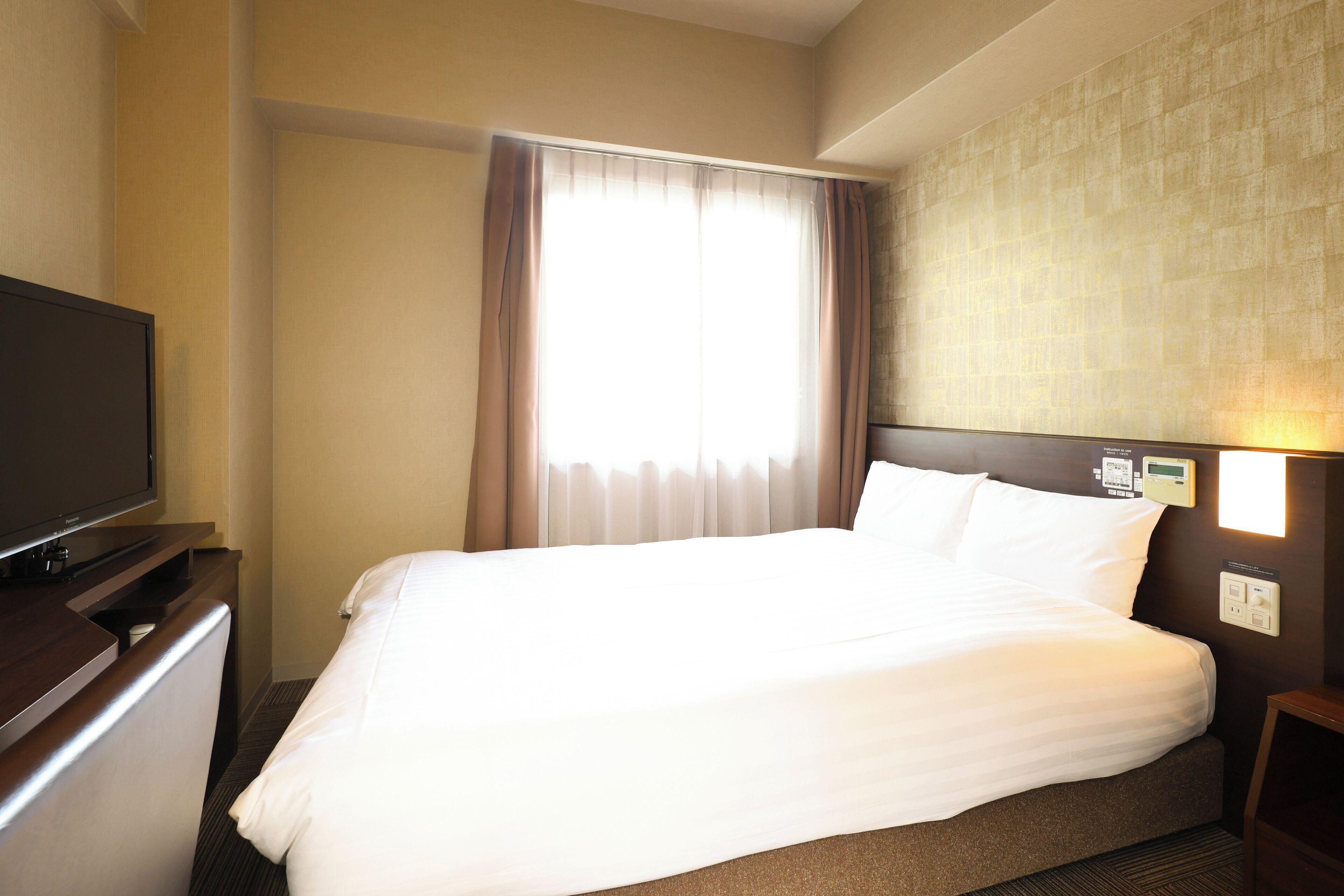 Una camera d'hotel con un letto grande, una TV a schermo piatto su una cassettiera in legno e un lampadario a parete.