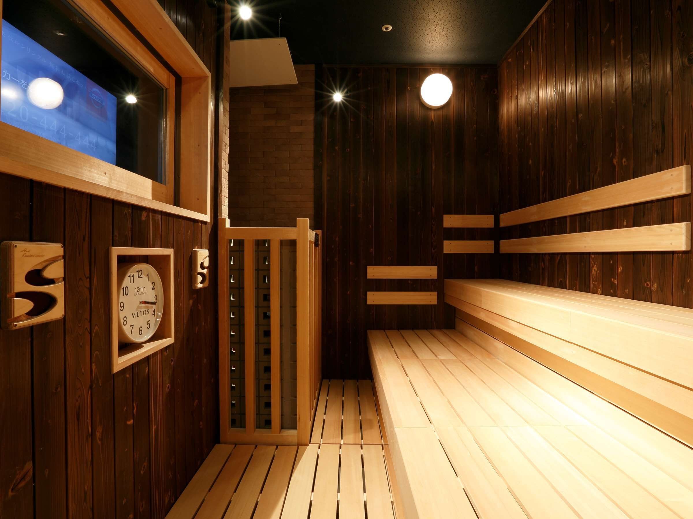 A sauna room with wooden benches, a clock, and a window.
