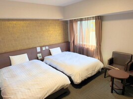 A hotel room with two beds, a small table, and a chair.