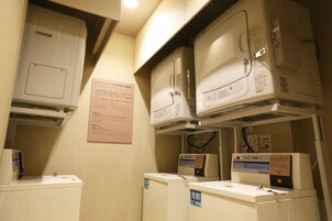 A laundry room with multiple washing machines and dryers, a control panel, and a sign with instructions.