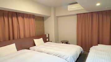 A hotel room with two beds, a small table, and an air conditioning unit.