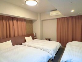 A hotel room with two beds, a small table, and an air conditioning unit.