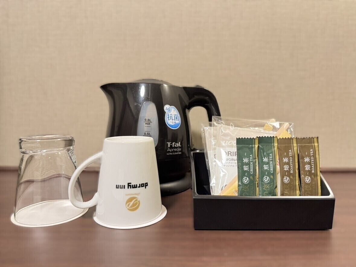 Eine Kaffeemaschine, eine weiße Tasse, eine Glas-Kaffeekanne und eine Packung Teebeutel.