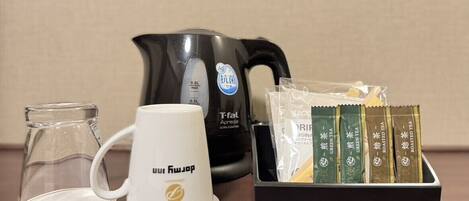 Eine Kaffeemaschine, eine weiße Tasse, eine Glas-Kaffeekanne und eine Packung Teebeutel.