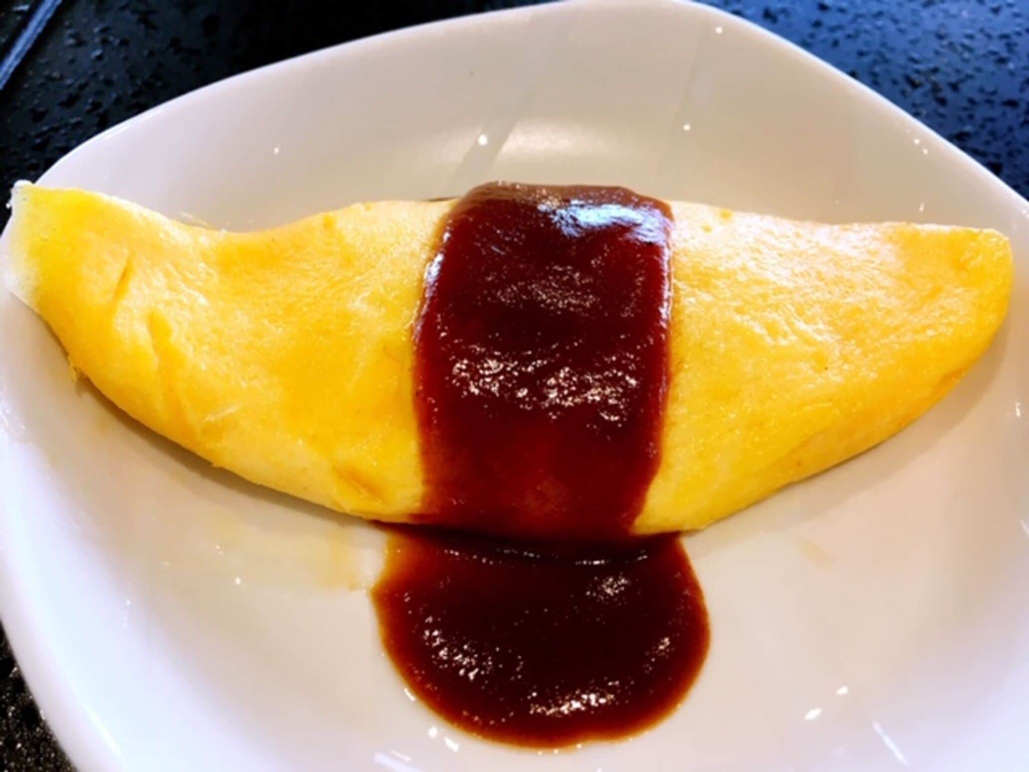 Un plato blanco con una tortilla enrollada y salsa oscura sobre una encimera negra.