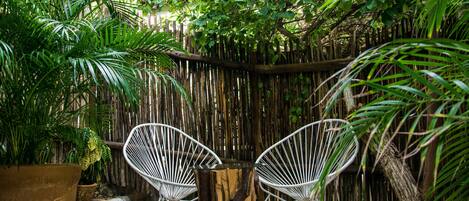 A garden area with two white wicker chairs, a wooden table, and a large potted plant.