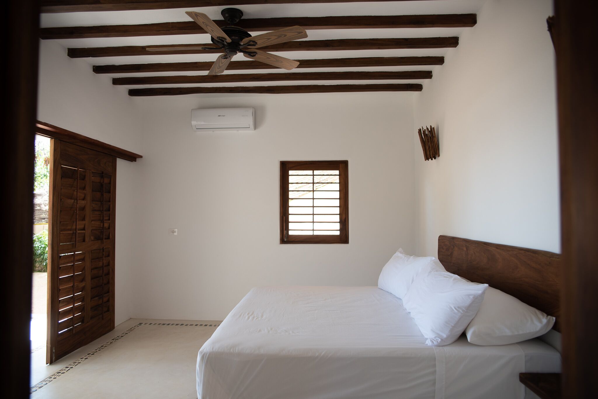 Un dormitorio con cama, vigas de madera en el techo, una ventana y un ventilador de techo.