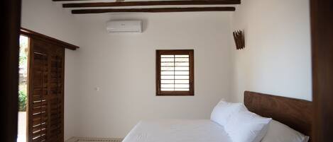 Un dormitorio con cama, vigas de madera en el techo, una ventana y un ventilador de techo.