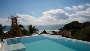 A clear blue pool with a view of the ocean and a thatched structure. - El Alquimista Yoga & Spa (San Pedro Pochutla)