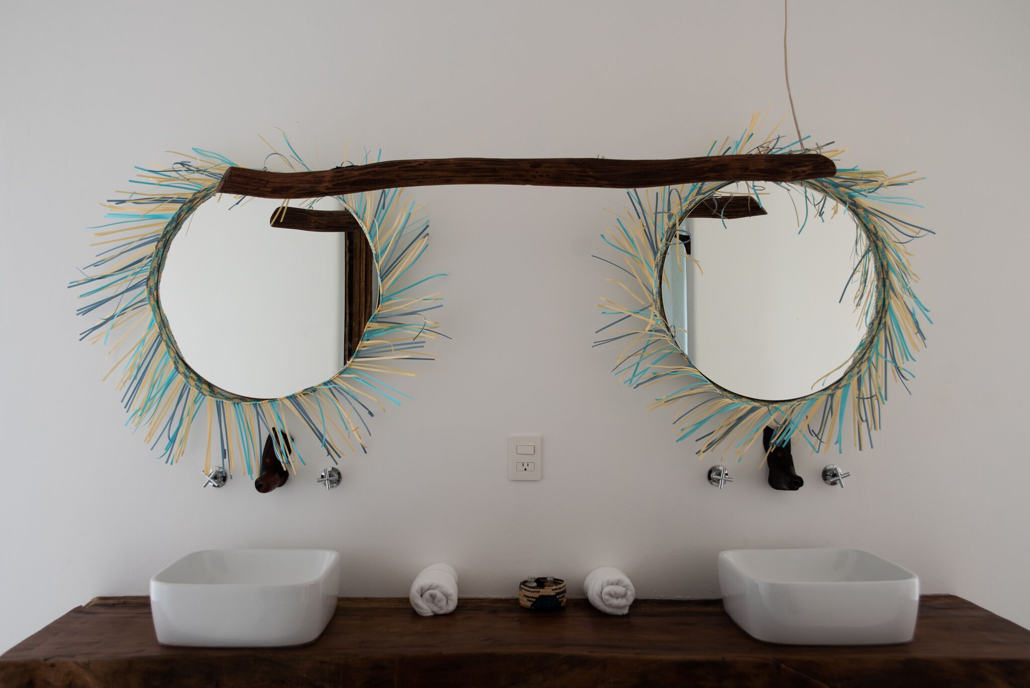 Ein Badezimmer mit zwei Waschbecken, einem Holzbalken über den Spiegeln und einer Steckdose.