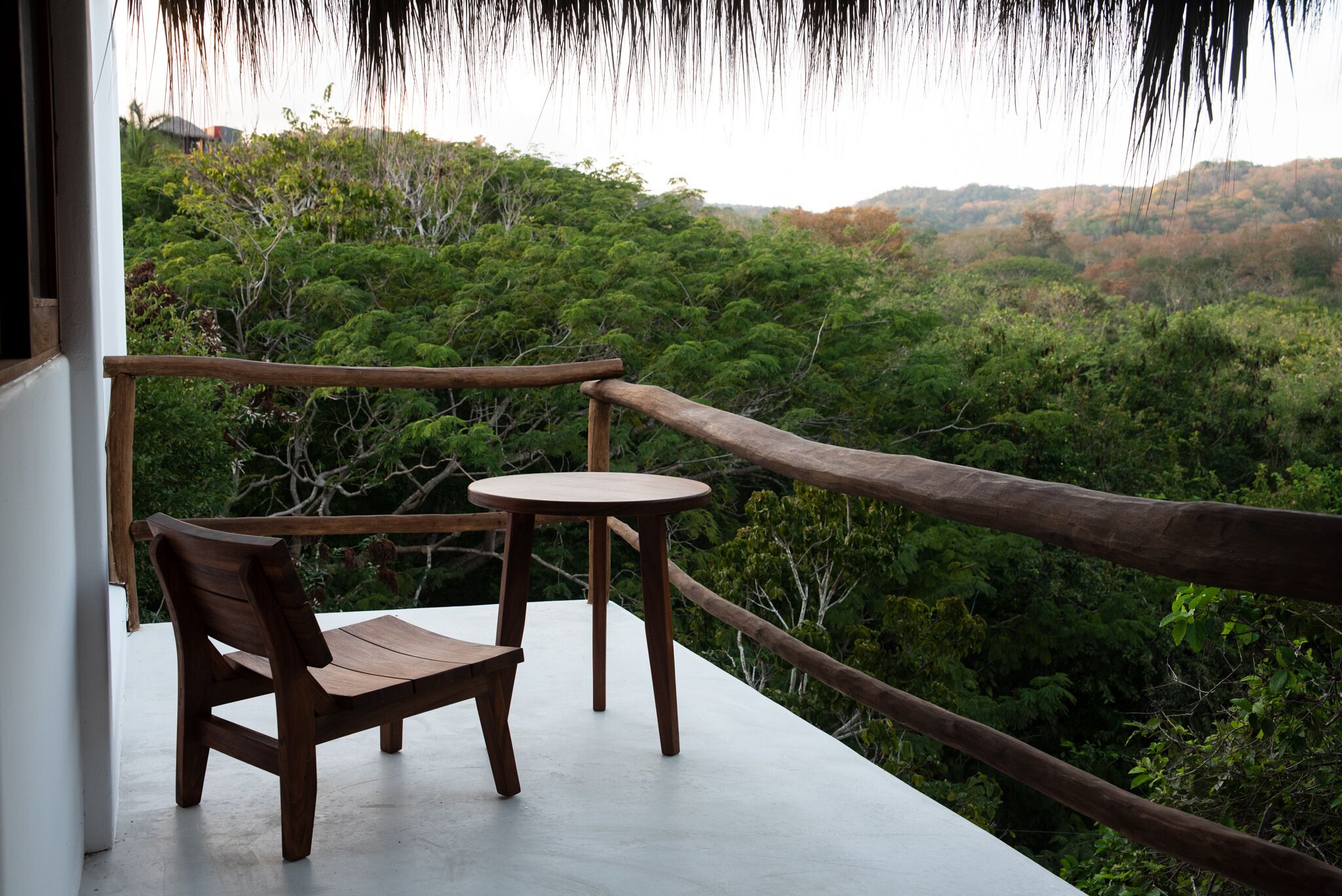 A wooden bench and table on a balcony with a view of a forested landscape.
